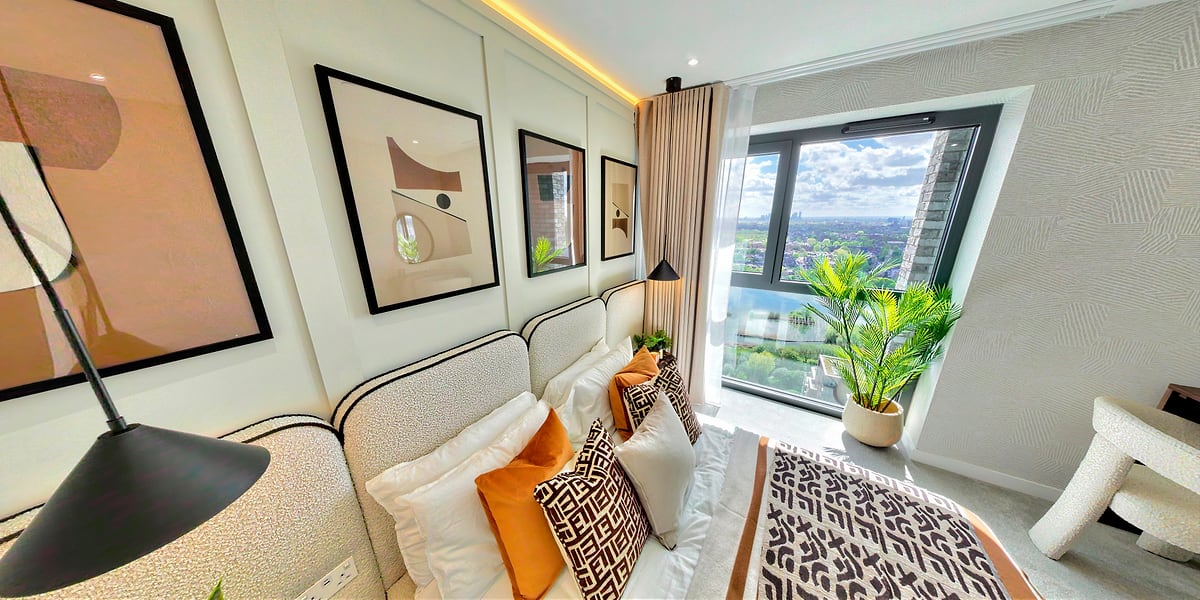 Master bedroom with framed art, warm cushions and a city view through full-height glass