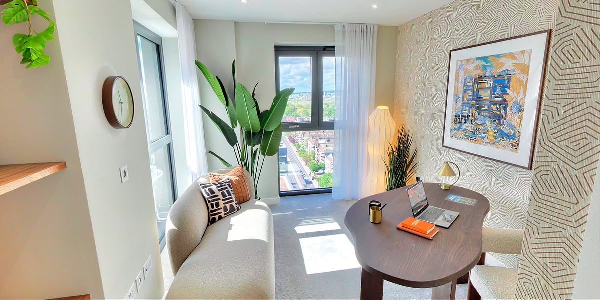 Study with grey sofa, framed artwork, plants and a writing desk
